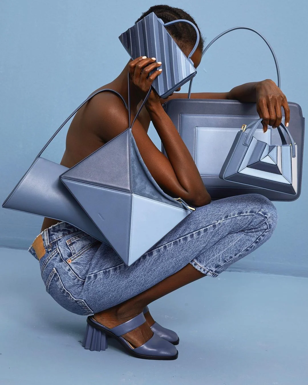A woman crouches while holding multiple blue handbags