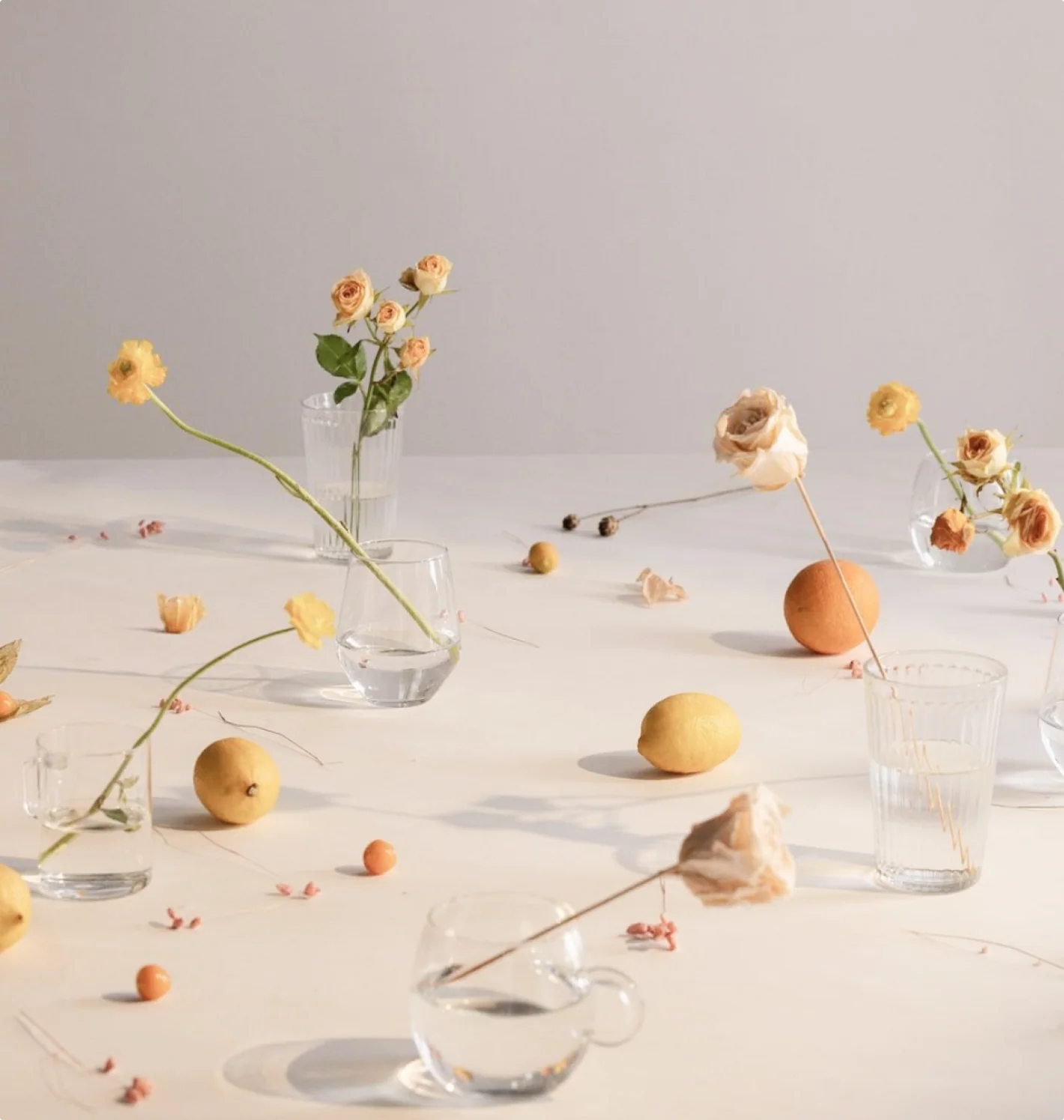 An assortment of glasses and cups holding flower stems. 