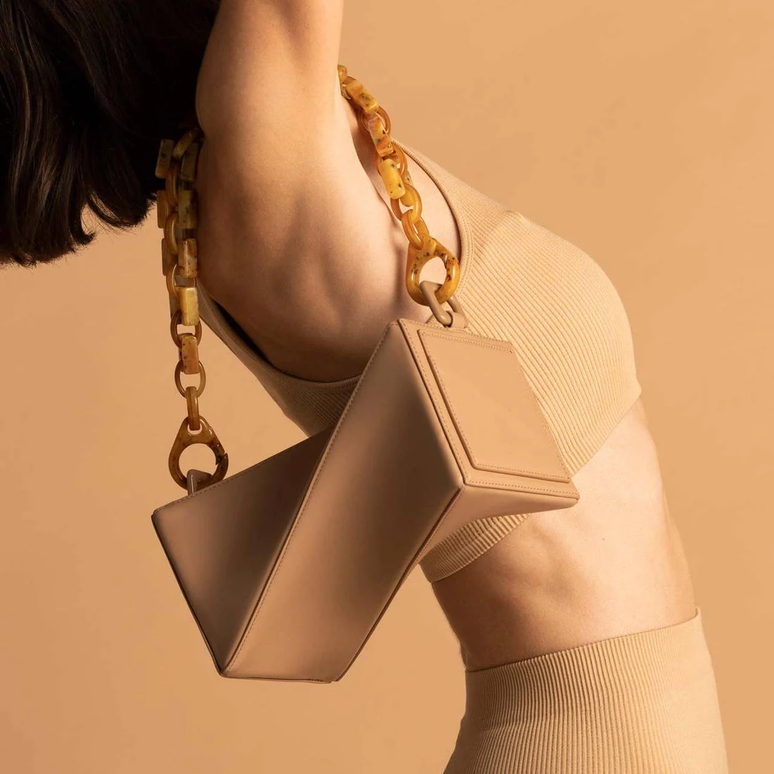 A woman wearing a beige cropped top models a beige handbag.
