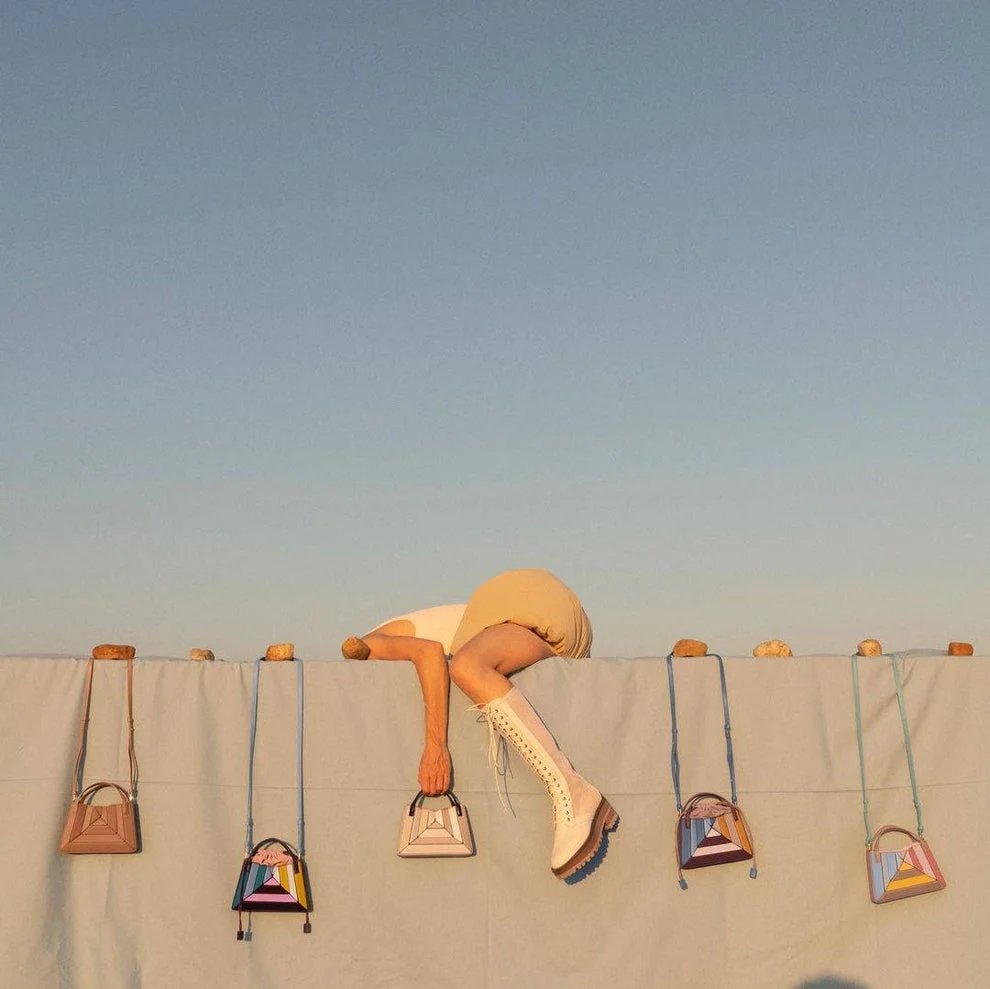 Several handbags hang against a cream colored outdoor wall. 