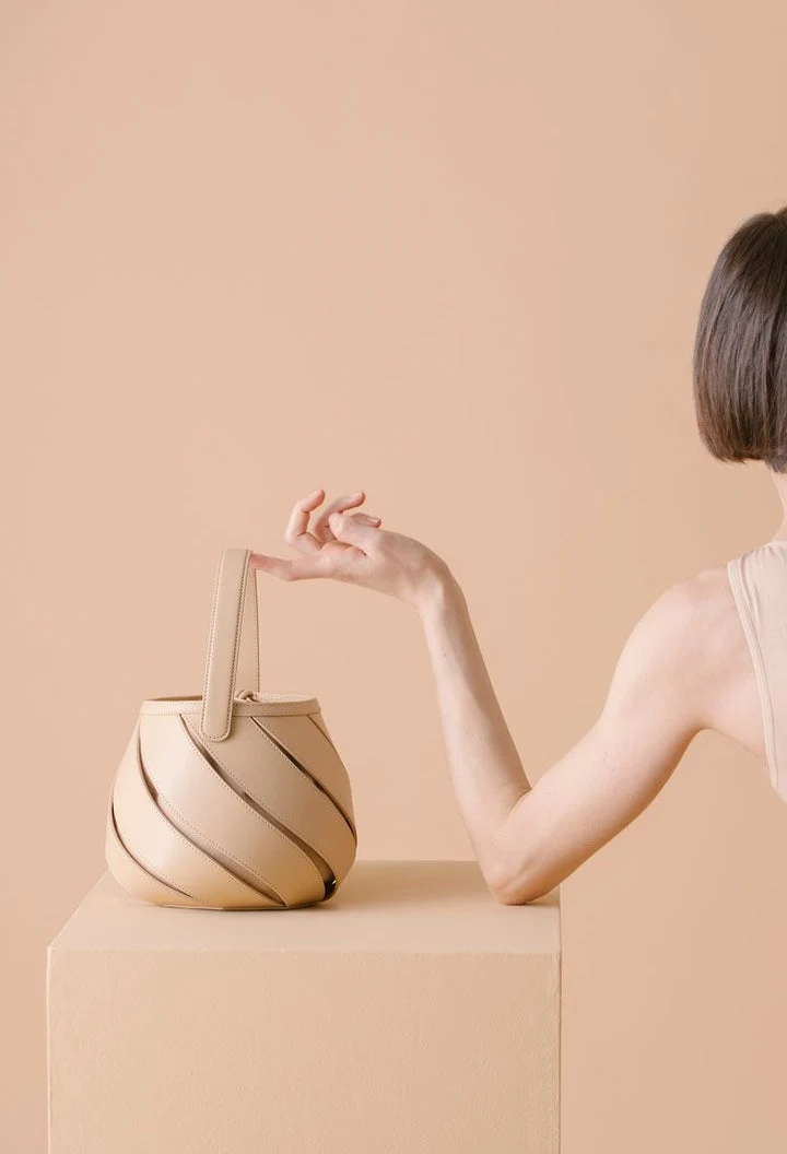 A light brown bag is displayed on a color-matched pedestal. 